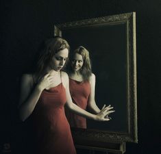 two women in red dresses are looking at their reflection in a mirror and one is holding her hand out