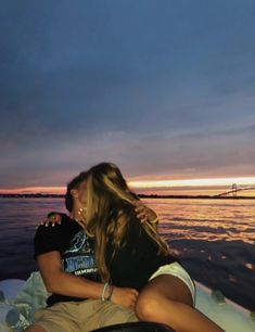 two people are sitting on a boat in the water at sunset or dawn, one is kissing the other's head