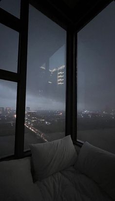 a bed sitting next to a window in a room under a sky scraper at night