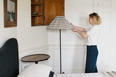 a woman is holding up a lamp shade in her living room while standing next to a bed