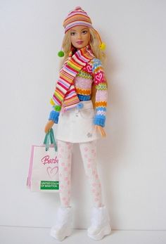 a barbie doll holding a shopping bag in her hand and wearing a colorful sweater with pom poms