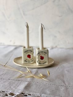 two white candles sitting on top of a plate