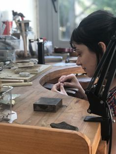 a woman sitting at a wooden table working on some kind of object in a workshop