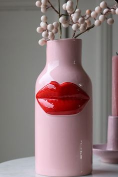 a pink vase with a red lip painted on the side and white berries sticking out of it