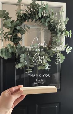 a person holding up a clear acrylic sign with greenery on it