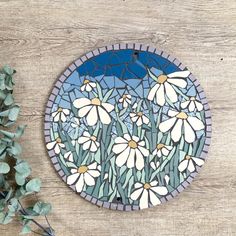 a blue and white stained glass plate with daisies on it next to a plant