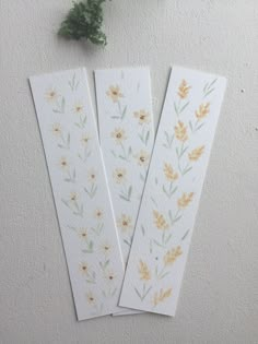 three bookmarks with watercolor flowers on them next to a green leafy plant