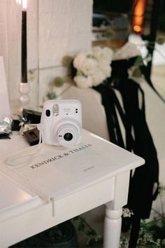 a white camera sitting on top of a table next to a vase with flowers in it