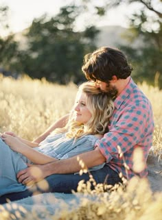 a man and woman sitting on the ground in tall grass looking at eachother