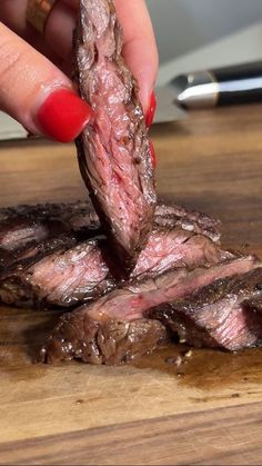 a woman's hand is picking up some steak