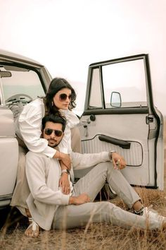 two people sitting on the back of an old car in front of a desert landscape