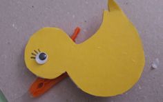 a yellow paper bird with orange scissors on the ground next to it's eyes