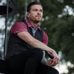 a man sitting on the edge of a stage with his hands in his pockets and looking off into the distance