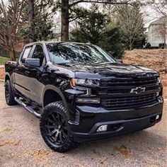 a black chevrolet truck parked on the side of a road in front of some trees