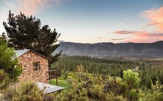 a small stone building sitting on top of a lush green hillside next to trees and mountains