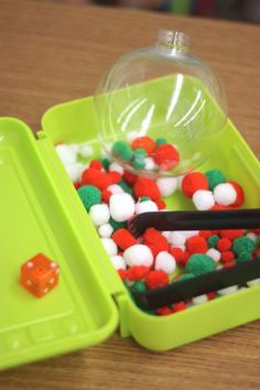 two green trays filled with different colored balls and plastic chopsticks on top of a wooden table