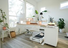 a white desk sitting on top of a hard wood floor next to a potted plant