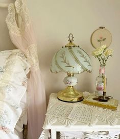 a white table topped with a lamp next to a bed