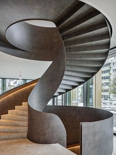 a spiral staircase in the middle of a room with large windows and concrete steps leading up to it