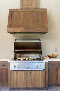 an outdoor bbq grill with wooden cabinets on the side and food cooking on top