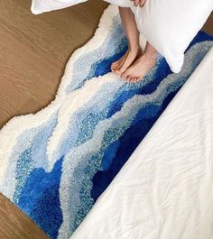 a person standing on top of a bed next to a blue and white wave rug