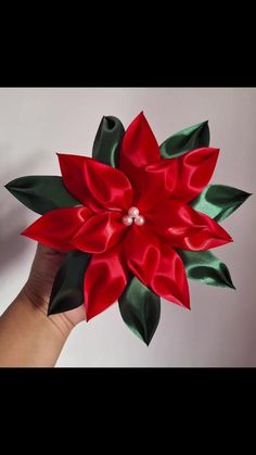 a hand holding a red and green poinsettia with pearls on it's center