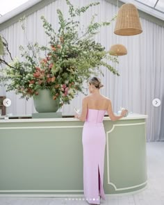 a woman in a pink dress is standing at the front of a reception counter with flowers