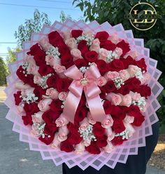 a person holding a large bouquet of red and pink roses in the shape of a heart