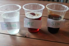 three plastic cups filled with liquid sitting on top of a wooden table