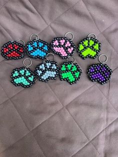 six beaded dog paw keychains with different colors and designs on them sitting on a quilt