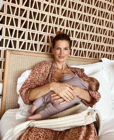 a woman holding a baby in her arms while sitting on a bed with pillows and blankets