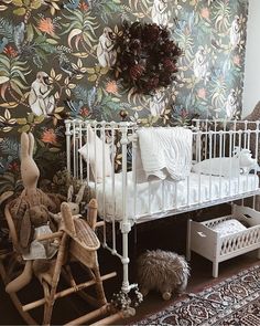 a white crib in front of a floral wallpaper and stuffed animals on the floor