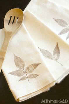 three napkins with leaves on them and a wooden spoon sitting next to one another