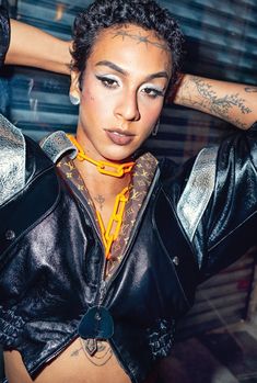 a woman with tattoos on her arms and chest wearing a black leather jacket, gold chain choker