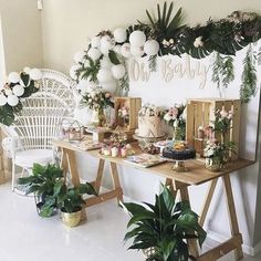 a table topped with lots of cake next to potted plants and balloons on the wall