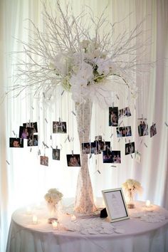 a table topped with a vase filled with white flowers and pictures hanging from the branches