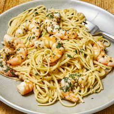 a plate of pasta with shrimp and parsley garnished with herbs, on a wooden table