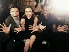 three people posing for the camera with their hands in the air and one person sitting on a chair