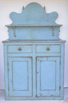 an old blue cabinet with two doors and one drawer on the top, sitting against a white wall