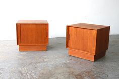 two small wooden cabinets sitting on top of a cement floor next to a white wall