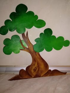 a wooden tree with green leaves sitting on top of a white floor next to a wall