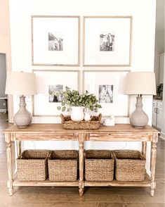 a wooden table with baskets on it in front of three framed pictures and two lamps