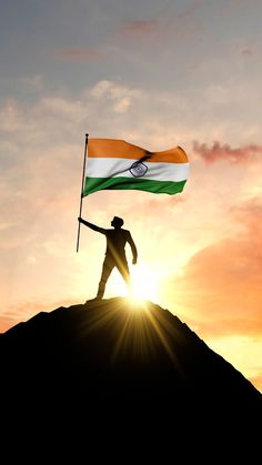 a man holding a flag on top of a hill with the sun in the background