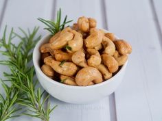 a white bowl filled with cashews next to a sprig of rosemary