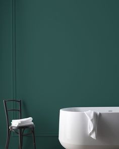 a white bath tub sitting next to a chair in a room with green walls and flooring