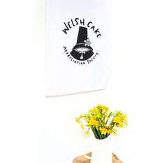 a vase filled with yellow flowers sitting on top of a wooden table next to a white wall