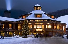 a lit up christmas tree in front of a large building with snow on the ground