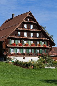 an old wooden house with green shutters and flowers in the window boxes on the roof