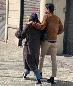 a man and woman walking down the street with their arms around each other's back