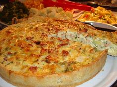 a large quiche on a white plate next to other foods